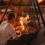 Traveller warming up by a campfire in a desert camp at night – Merzouga, Morocco