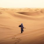 Guide in traditional clothes walking through the dunes – Merzouga, Morocco