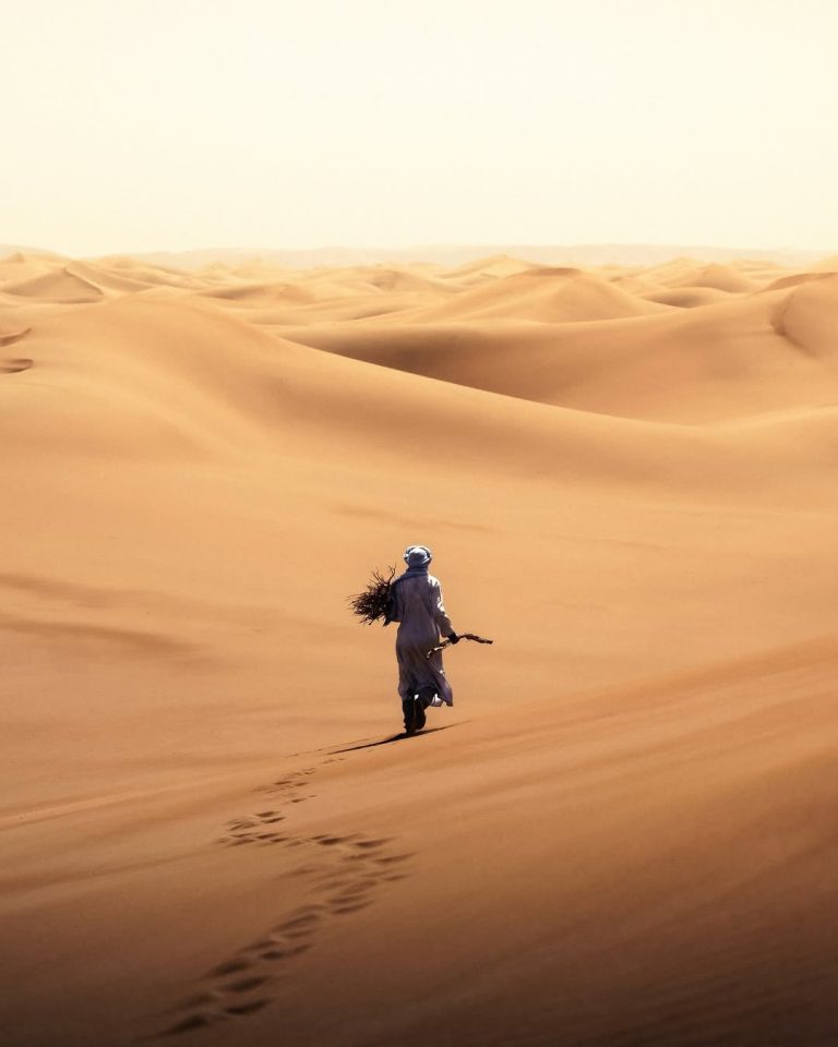 Guided Walking Tour Guide in traditional clothes walking through the dunes – Merzouga