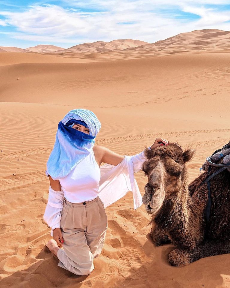 Traveller in a blue scarf with a camel in the dunes – Merzouga