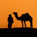 Silhouette of a camel and guide at sunset – Merzouga, Morocco